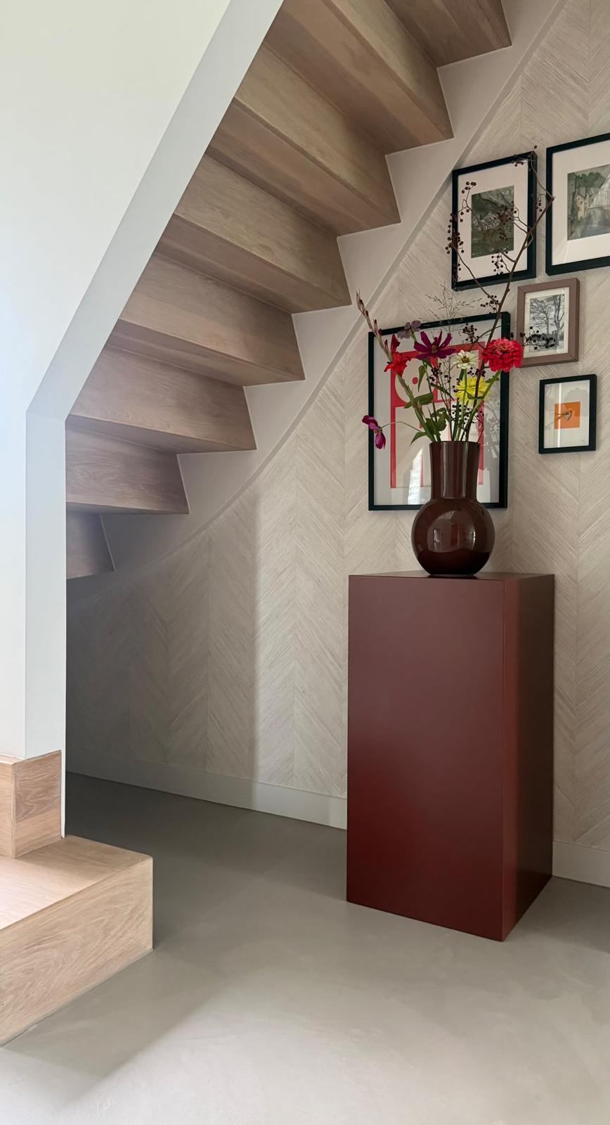 Bordeauxrode MDF pilaar met een vaas bloemen onder een houten trap