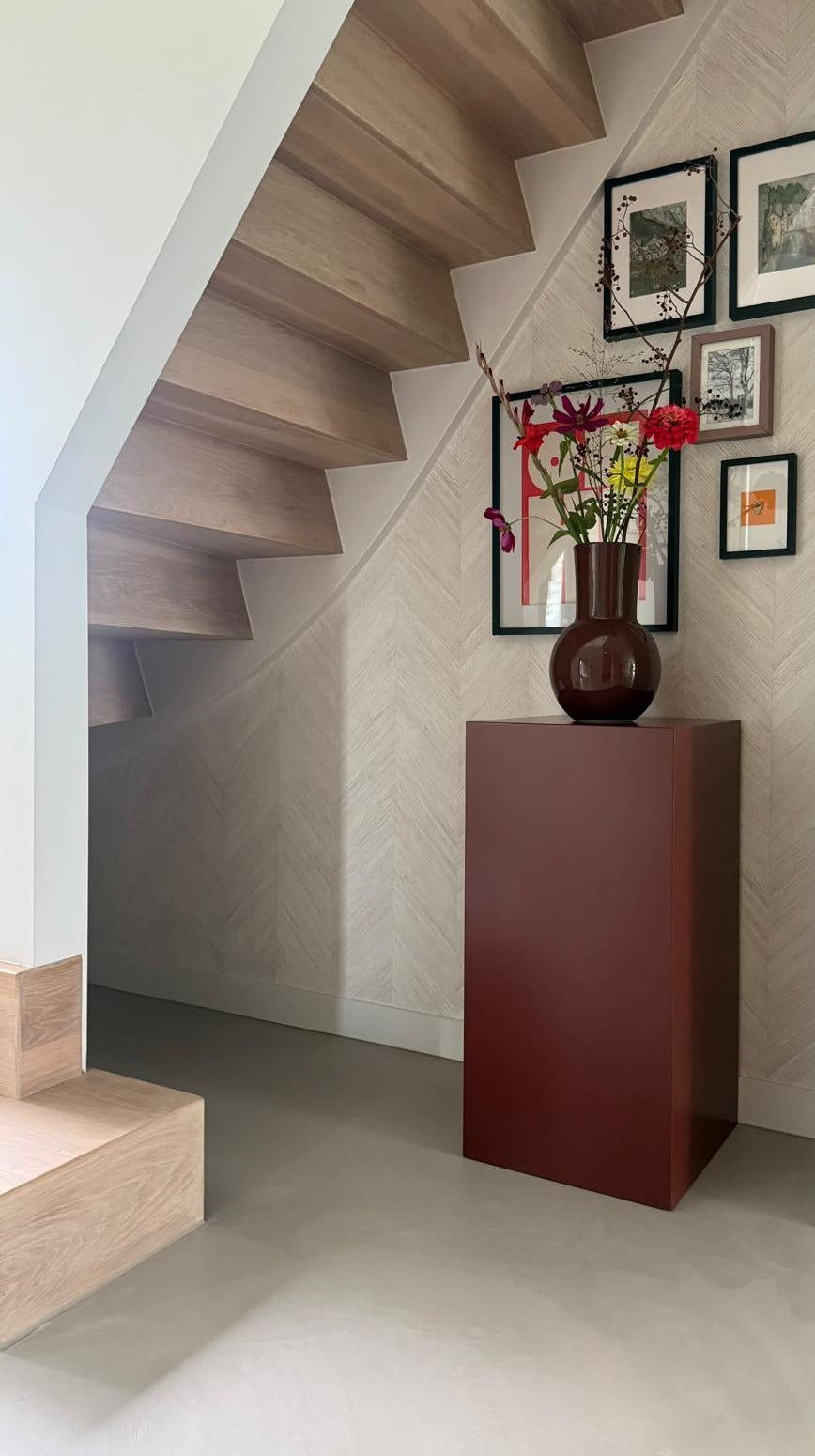 MDF pilaar 40 x 40 x 80 cm in de Bibelotte-kleur Merlot, met een vaas bloemen onder een trap in een hal