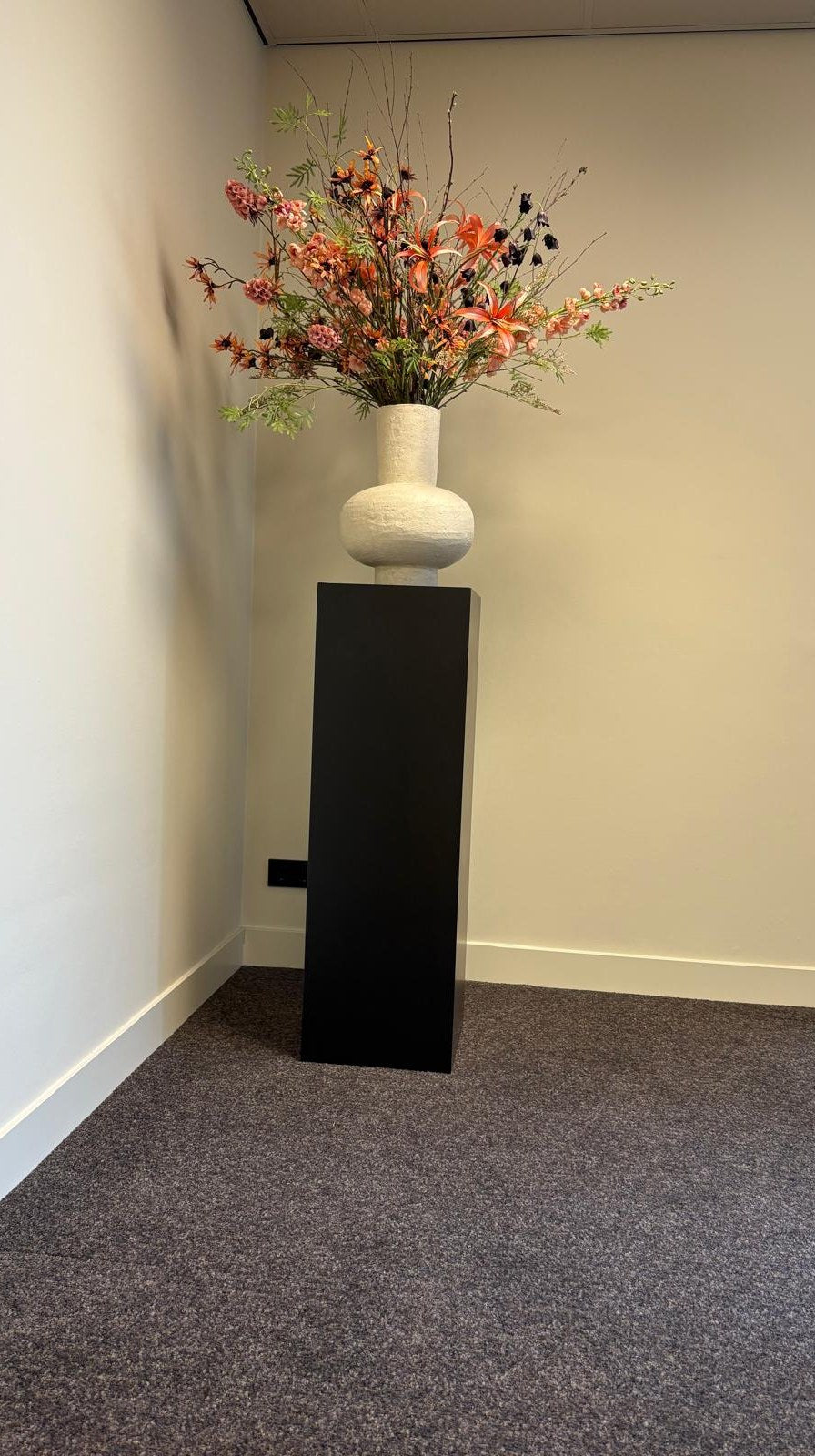 Zwarte MDF pilaar op maat, 35 x 35 x 110 cm, met een grote vaas in een kantoorhoek